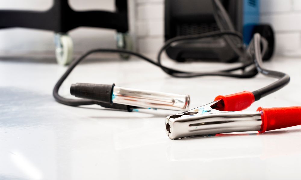 Pinzas de la batería del coche con cables de color rojo y negro para polos positivo y negativo sobre una mesa de trabajo de color blanca.