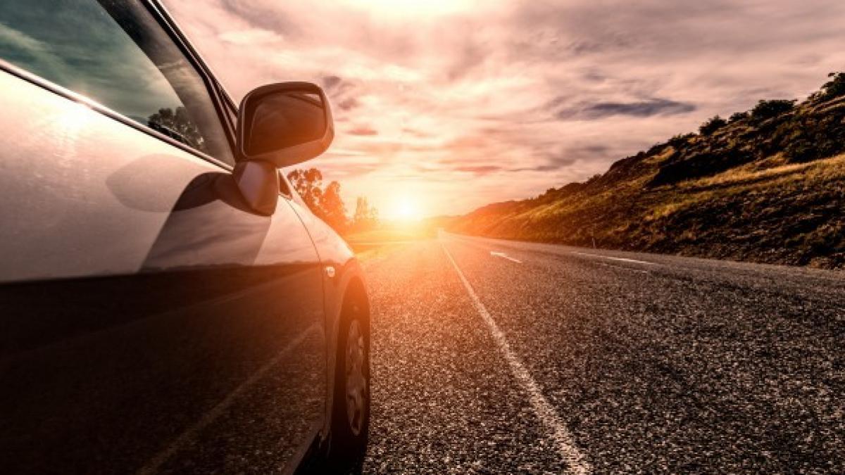 Fotografía frontal de una carretera de asfalto soleada al horizonte y un coche en paralelo que va conduciendo en dirección al sol |Mycaready