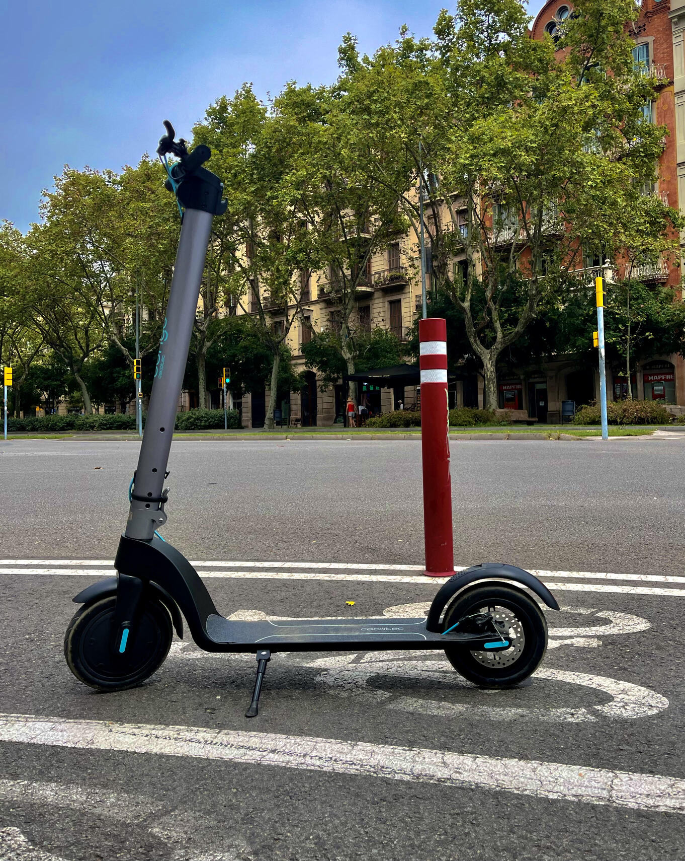 Patinete eléctrico en un carril bici con árboles y semáforos de fondo ubicado en Passeig Sant Joan, en el centro de Barcelona.