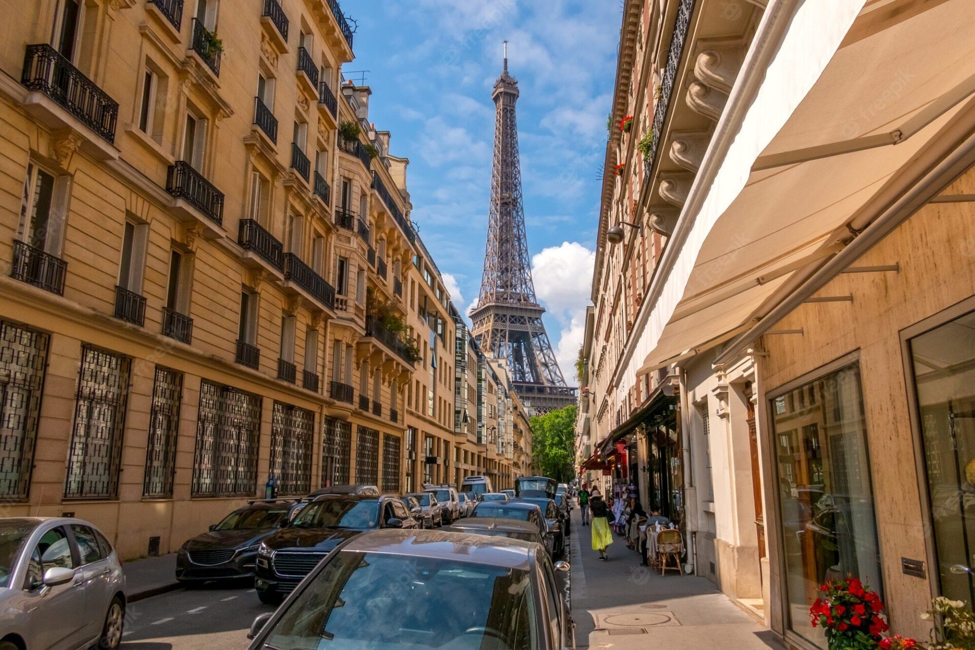 Imagen interior de una calle de un solo carril en París llena de coches aparcados a los dos lados y donde al final se puede ver la Torre Eiffel de fondo.