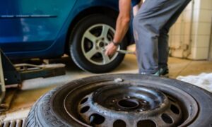 Imagen de cerca de un neumático nuevo y en el fondo un mecánico reparando el neumático de un coche | Mycaready Technologies