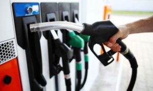 Imagen de cerca de cuatro surtidores de gasolina y diésel en una gasolinera convencional donde la mano de un hombre está a punto de dejar la primera manguera en su sitio.