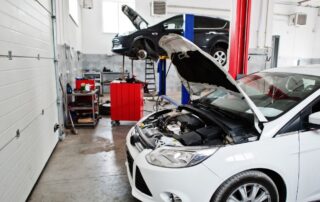 Sala de un taller mecánico en el que se están reparando dos vehículos, uno de los cuáles tiene el capó levantado esperando por revisión.
