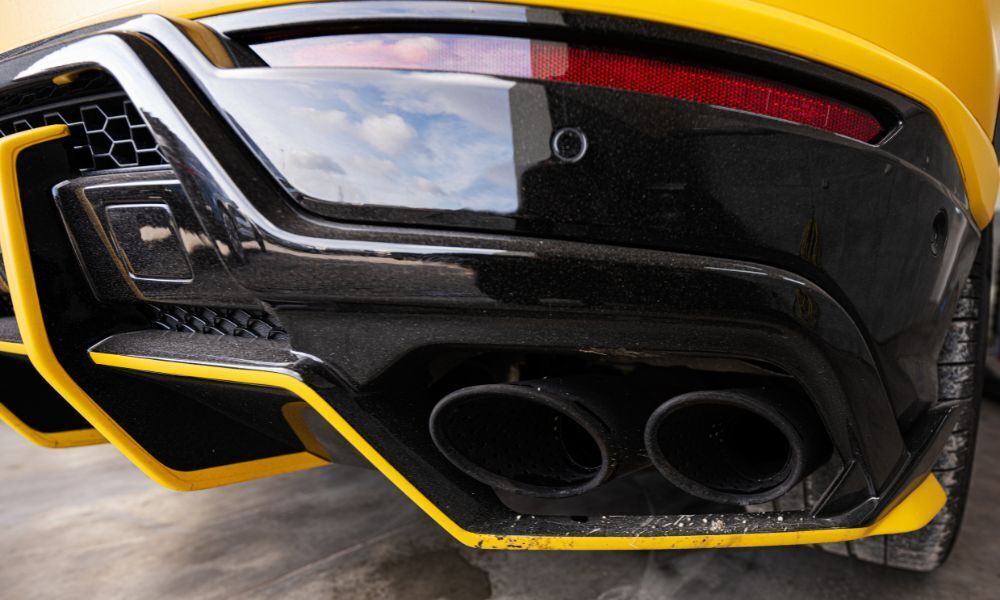 Foto detalle del doble tubo de escape de un coche deportivo color amarillo, ejemplo de coches a combustión que estarán prohibidos a partir del 2035.