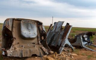Imagen de varias piezas de coche oxidadas y abandonadas en un desguace en medio del campo.