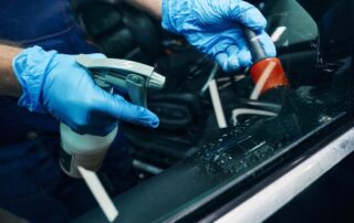 En el taller mecánico, manos de un mecánico utilizando guantes para poner un producto de limpieza en un coche. | Mycaready Technologies