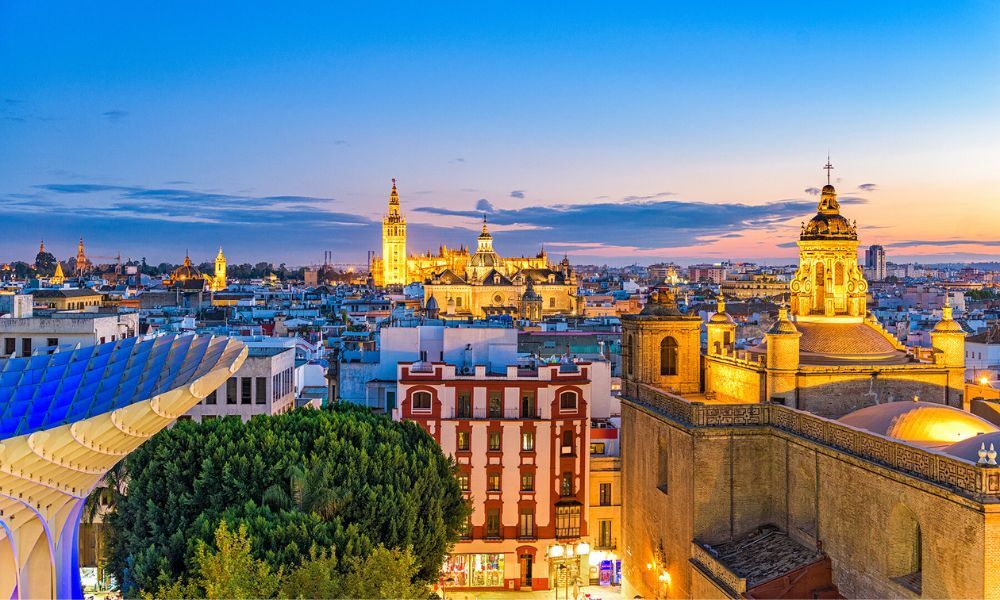 Imagen desde arriba de la bonita ciudad de Sevilla iluminada y colorida mientras el sol se pone a lo lejos en plena estación de verano.