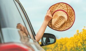 Mujer sujetando un sombrero con su mano fuera de un vehículo en marcha, luego de hacer una revisión de mantenimiento a su vehículo en verano.