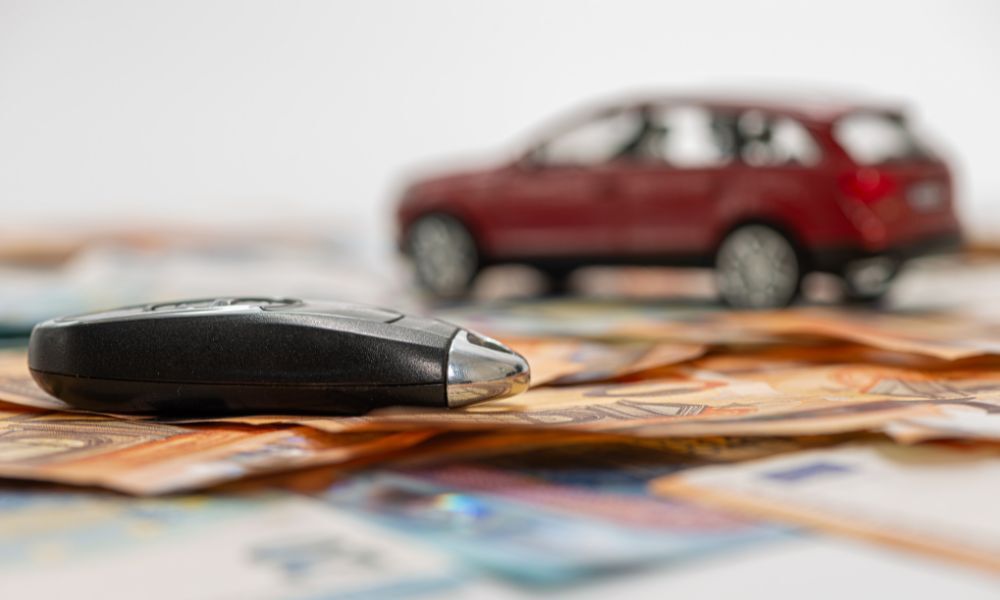 Detalle de las llaves de un vehículo sobre unos billetes de Euro, el fondo se ve un todoterreno para ilustrar la publicación vender coche financiado.